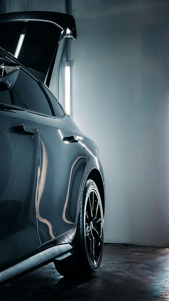 A modern luxury car with open trunk in a dimly lit indoor garage, showcasing its sleek design.
